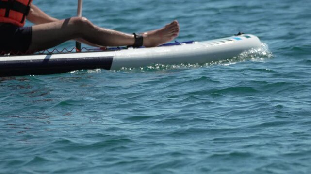 Paddleboarding kayaking ocean paddler using oar on surfboard while sitting on sea surface during sunny summer day for recreation and water sports activity