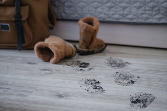 Muddy footprints on laminate floor with dirty children's boots indoors. Rainy day home cleaning concept