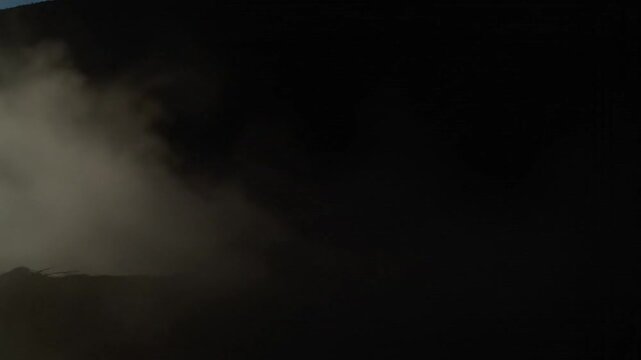 Dense gray smoke billows against a dark and moody background