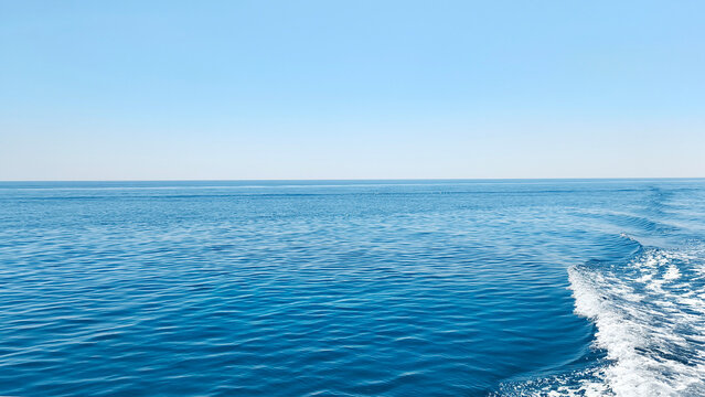 Calm blue Mediterranean Sea with gentle boat wake under a clear sky. Peaceful seascape, travel destination, summer vacation and open water background.