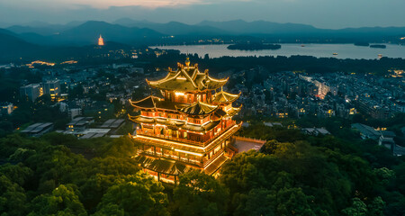 Fototapeta premium Aerial landscape of West Lake Hangzhou at dusk, tranquil lake with tree causeway, city skyline and Leifeng Pagoda in distance, Chinese natural scenic spot
