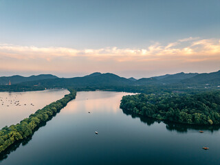 Fototapeta premium Aerial landscape of West Lake Hangzhou at dusk, tranquil lake with tree causeway, city skyline and Leifeng Pagoda in distance, Chinese natural scenic spot