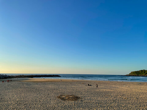 Sunset view of Zurriola Beach in San Sebastian, Spain. Golden sand, Atlantic waves, blue sky and people by the sea.