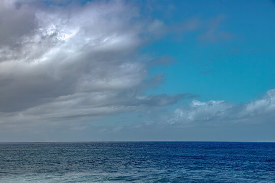 Blue ocean horizon under dramatic sky with heavy clouds creating serene and expansive atmosphere