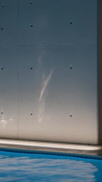 Water caustic reflections dancing on a concrete wall by a swimming pool, sunlight projecting patterns and ripples on a modern architectural surface creating an abstract effect