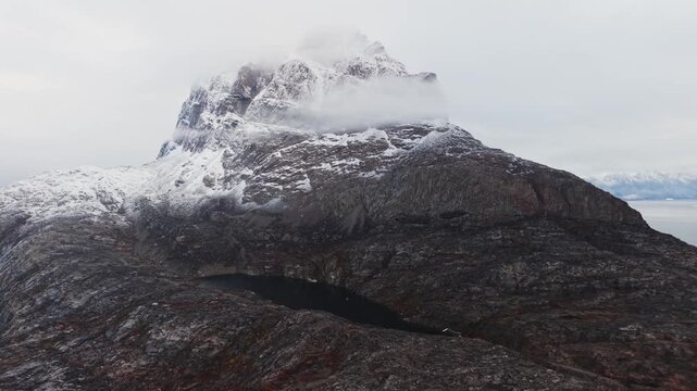 Aerial Cinematic View of Giant Snowy Mountain Peak and Dark Glacial Lake