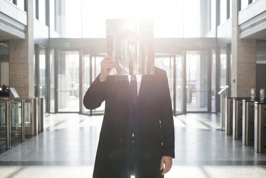Businessman Hiding Face Behind Mirror in Office Lobby