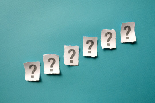 Diagonal line of six white paper notes with question marks on solid blue surface for options