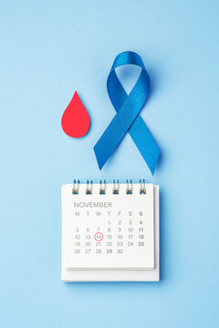 Blue ribbon with red blood drop and November calendar with mark on 14 on light blue background, World diabetes day awareness