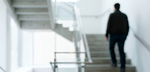 Fototapeta premium A person walking up a set of modern concrete stairs in a bright, minimalistic environment. The focus is soft, creating a sense of depth and motion.