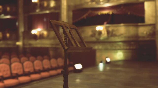 Close music stand under warm spotlight, sheet music clips visible, shallow depth of field capturing amber glow on metal stand and distant plush rows, intimate