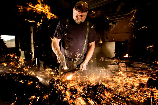 Blacksmith working with hammer at anvil surrounded by sparks