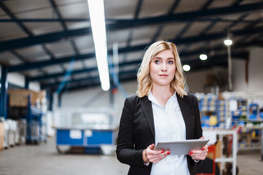 Blond businesswoman standing in shop floor, using digital tablet