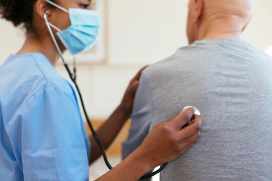Doctor using stethoscope for listening to patient's heartbeat at home