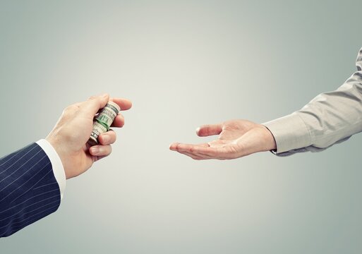 Hand giving rolled bribe money to receiving hand for illegal payment
