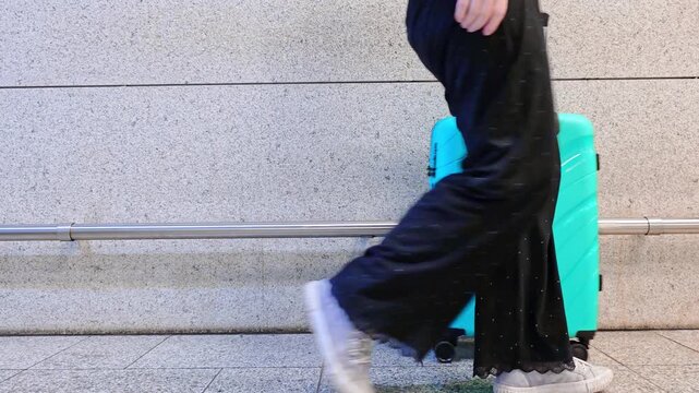 Woman rolling teal hard-shell suitcase across airport floor, travel lifestyle, airport arrival, solo female traveler.