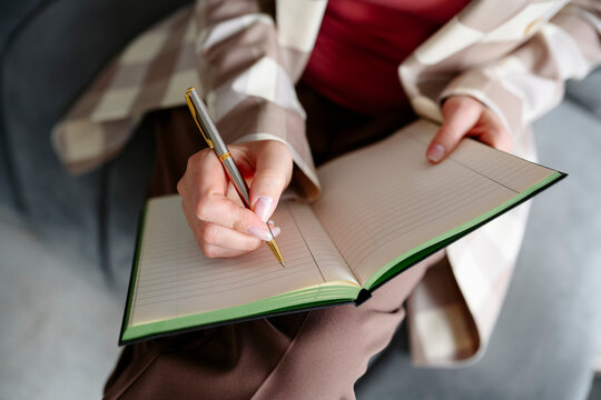 Close-up of hands writing with a pen in a blank notebook