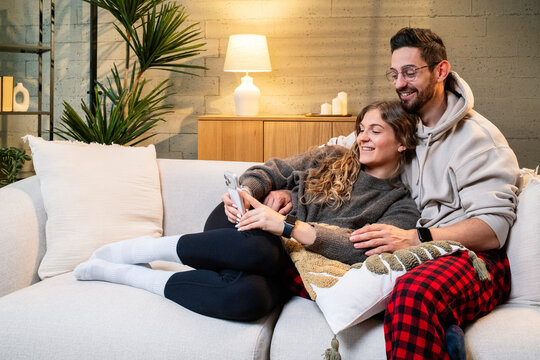 Smiling couple taking selfie on sofa in cozy living room