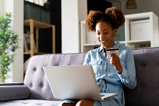 Smiling woman paying through credit card using laptop in living room