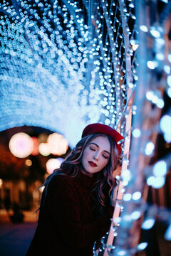 Model wearing a red beret leaning on festive string lights at night