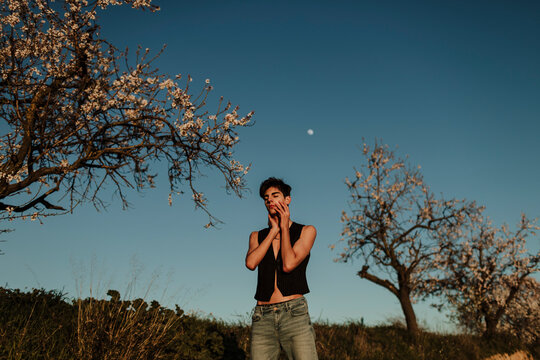 Young man standing outdoors with eyes closed near blossoming trees