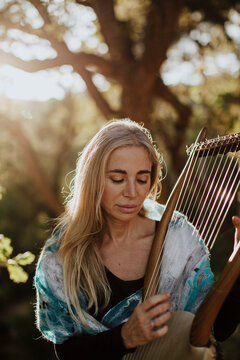 Musician playing a harp outdoors in a sunny forest