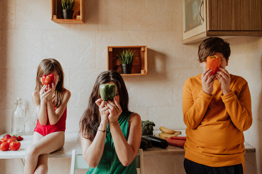 Family holding bell pepper over face in home kitchen