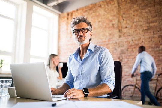 Businessman using laptop in office with colleagues in background