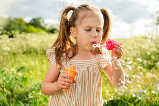Daughter blowing soap bubble in sunny summer meadow