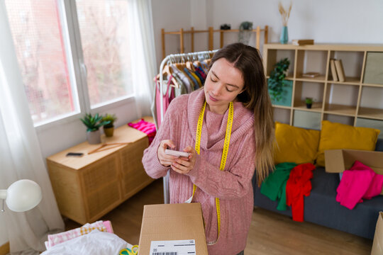 Entrepreneur scanning cardboard box with smartphone at home office