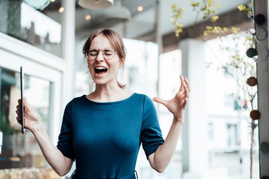 Frustrated businesswoman screaming while holding digital tablet in cafe