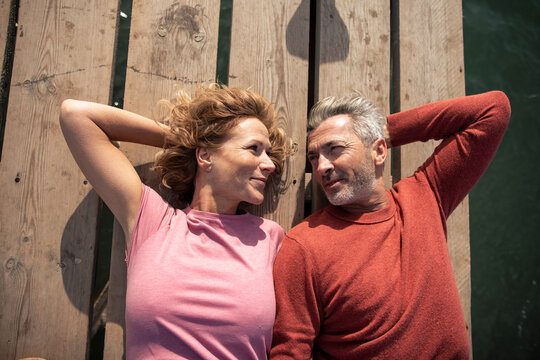 Smiling mature couple lying on jetty floorboard