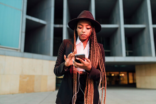 Businesswoman with smart phone listening music through in-ear headphones outside office building