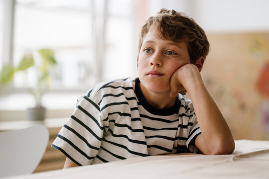 Bored boy sitting at table daydreaming indoors