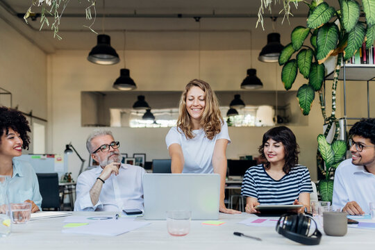 Smiling businesswoman planning strategy on laptop with coworkers in office