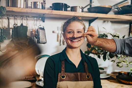 Chef making mustache of dry chili to colleague while standing in kitchen
