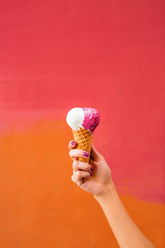 Woman's hand holding ice cream in front of colourful backgound