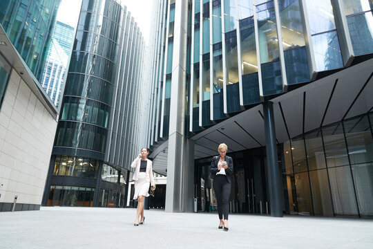 Female entrepreneurs walking with smart phones against office building at downtown district in city