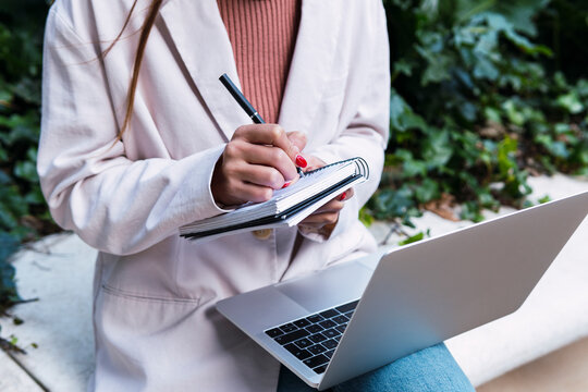 Businesswoman writing in diary sitting with laptop at park