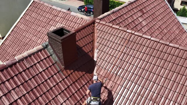 Roof renovation process with spray painting of roof tiles, including priming and applying second coat of paint on a residential roof, showing professional exterior maintenance and refurbishment work.