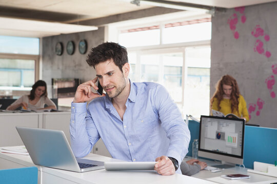 Portrait of man with laptop telephoning with his smartphone in the open space office