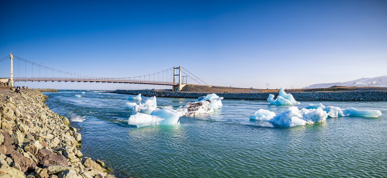 Blue icebergs drift under a suspension bridge at J�kuls�rl�n lagoon
