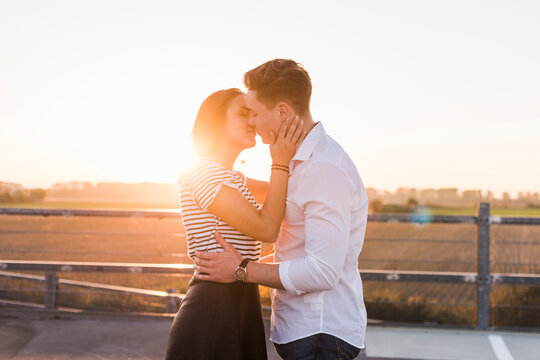 Young couple kissing on parking level at sunset