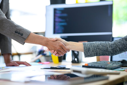 Software Developers Sealing a Business Deal with Handshake in Tech Office with Code on Monitor