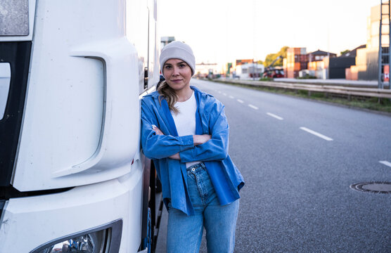 Confident woman truck driver leaning on semi truck outdoors