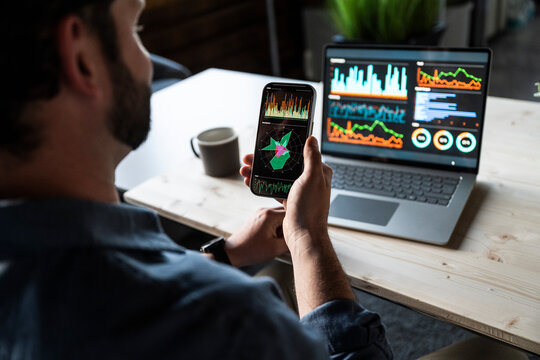 Professional analyzing financial data on smartphone and laptop