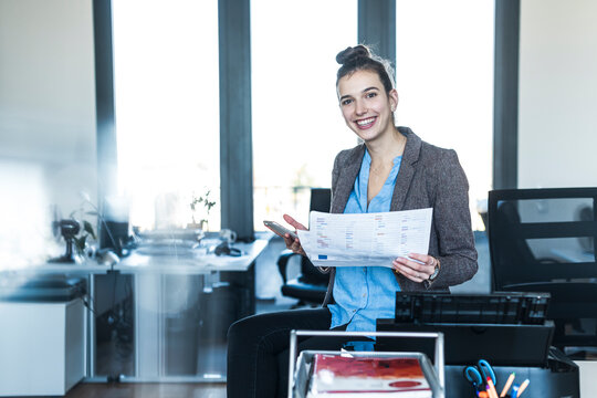 Smiling businesswoman holding document and phone in office