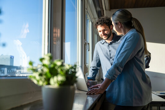 Business professionals brainstorming with laptop by office window