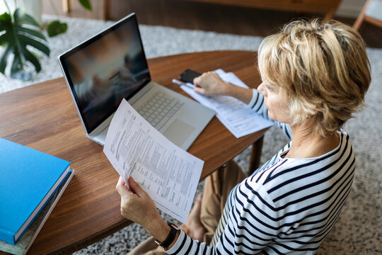 Mature woman with documents using laptop at home