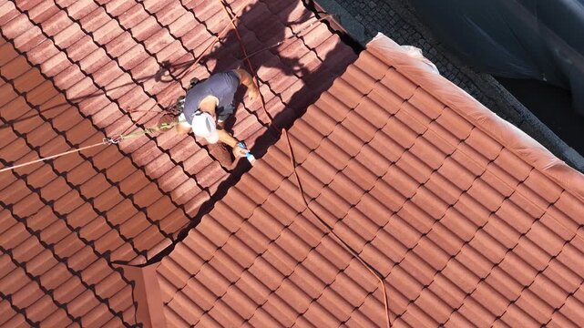 Roof renovation process with spray painting of roof tiles, including priming and applying second coat of paint on a residential roof, showing professional exterior maintenance and refurbishment work.